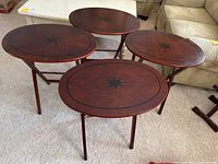 Four oval wooden folding tray tables arranged standing with visible compass rose design and dark wood finish