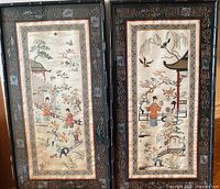 Two embroidered silk panels side by side, framed in dark wood with decorative painted designs, showing traditional Asian Geisha and landscape scenes embroidered in silk.