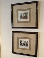 Photo showing both framed prints mounted vertically on a wall: one above the other, framed in dark wood with beige mats.