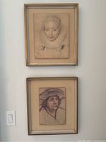 Two framed vintage reproduction artworks mounted on board hanging on a wall, one above the other.