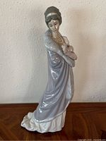 Front view of the porcelain figurine showing the lady in a long lavender and white coat with a fur collar and pearl necklace.