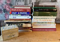 Photo of a stack of vintage cookbooks including 'Sugar Busters!', 'Thoughts for Buffets', 'Abe's Goody', 'Year Round Holiday', 'Cooking for Entertaining', and other assorted titles. Also two decorative metal recipe tins at the front.