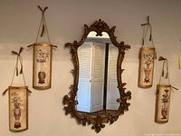 Full view of wall hanging mirror and four curved wood panels with painted urns hung on the wall.