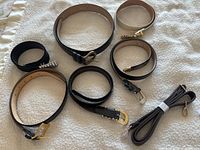 Overview of all 7 belts and one purse strap laid out on fabric surface, showing various buckle styles and leather colors.