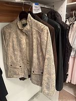 Front view of Alfani beige snake print moto jacket hanging on rack with other jackets and vests