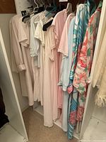 Collection of various women's nightgowns and silk robes hanging on hangers showing a range of pastel and floral patterns.