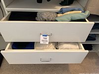 Three open drawers showing folded women's sweaters, tops and pants in various pastel colors and textures.