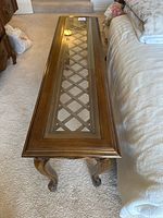 Top and side angle showing glass panel with lattice weave underneath and decorative carving on legs.