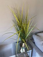 Full view of artificial grass plant in metallic pot beside sofa