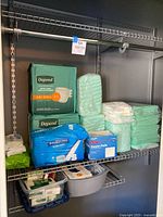 Shelf with Depend diaper packs, loose green briefs, wipe pack, FitRight underwear pack, gauze pads, underpads bag and basin
