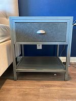 Front view of grey metal nightstand showing drawer and shelf