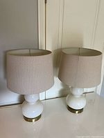 Two matching white ceramic table lamps with beige drum shades displayed on table