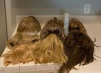 Seven wigs of varying colors and one hairspray can on countertop