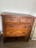 Front view of stained wood four-drawer dresser with metal pulls and bottom shelf
