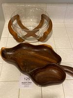 Wooden two-section bowl and glass bowl in wooden stand on tiled surface