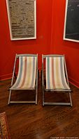 Two vintage wooden lounge chairs with multicolor vertical striped fabric seats and backs against a red wall, showing the front view.