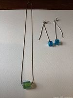 Full view of necklace and dangle earrings on flat surface showing glass beads and silver chain/earring posts