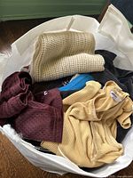 Top view of bag showing folded clothing items including knit sweaters and ribbed shirts in lighter and darker colors.