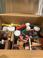 Box filled with assorted vintage wooden rubber stamps, glue tubes, paint tubes, and other art supplies