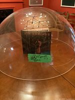 A large clear acrylic dome placed on a wooden table, showing the dome's size relative to a book inside it.