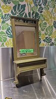 Front view of green wood wall mirror with built-in shelf, showing decorative top and shelf details.