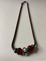 Full view of the silver necklace with central cluster of red and white beads on woven chain.