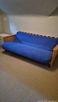 Full view of futon sofa with blue cover and wood frame under soft lighting.
