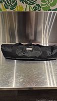 Black nylon carrying bag with zippered closure shown on metallic surface, appears in good condition.