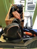 Wide view showing basket filled with baseball gloves, helmet, goggles, balls, and badminton rackets.