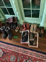 Wide view showing 12 pairs of women's shoes mostly size 7, including boots and various heels and flats arranged on floor by windows.