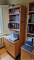 Front angled view of the tall wooden bookcase with shelves filled with books and papers, and closed cabinet doors below.