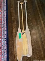 Three wooden canoe paddles laid out on a wooden floor showing size and condition.
