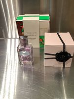 Viktor&Rolf Flowerbomb boxed, Prada perfume bottle, and L'Occitane Almond cream travel set, displayed on metallic surface.