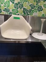 White molded plastic chair shell on a metal countertop with green painter's tape attached showing measurements and condition.