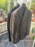 Two blazers hanging on rack in sunlit room showing overall front view