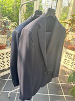 Two suit jackets on a clothing rack in a sunlit room with plants