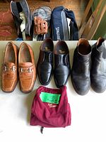 Three pairs of men's leather shoes: brown crocodile-textured loafers, black leather oxfords, black leather boots displayed with Allen Edmonds shoe bag