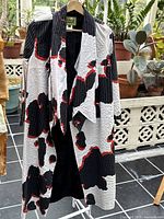 Front view of the kimono coat hanging on a stand with visible abstract floral patterns in black, red, and a striped white background.