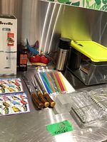 Overview of all items in lot on stainless steel surface, including boxed sous vide cooker, pepper grinder, carving utensils, reusable eco-friendly straws, thermos and decorative kitchen items.