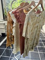 Four silk tops and a jacket hanging on rack showing multiple floral dyed designs in soft natural earthy colors.