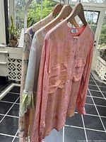 Three silk tops hanging on wooden hangers showing colors and hand-dye floral patterns.