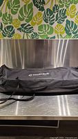Black carry case with Canadian Studio logo on stainless steel table under decorative green leaf wall.
