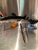 Wide view of all four wooden fish sculptures showing display setup on a metal surface, detailed paint on large fish and polka-dotted fish, smaller two black fish pieces in front.