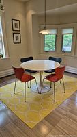Front view of round white tulip table with five chairs on yellow rug