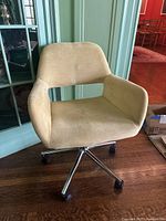 Front-side view of beige upholstered office chair showing fabric condition, armrest design, and chrome metal base with casters.