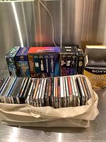 Photo showing a bag filled with multiple CDs and VHS boxed sets arranged behind it.