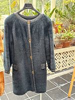 Full front view of the black fur coat hanging against a background showing plants and tiled floor.