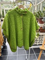 Front view of green wool cape on hanger showing button closure and collar.