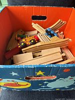 Box filled with wooden train track pieces and a red fire truck car visible on top.