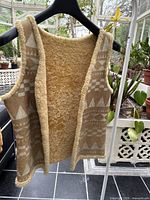 Front and inside view of vest hanging on black hanger with geometric pattern and Sherpa lining.